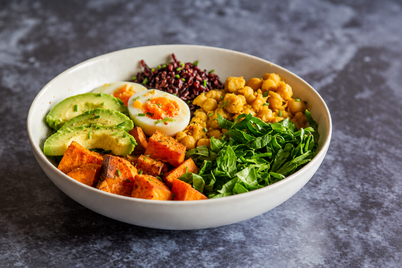 A nourishing bowl with avocado, eggs, chickpeas, rice, sweet potato, and leafy greens